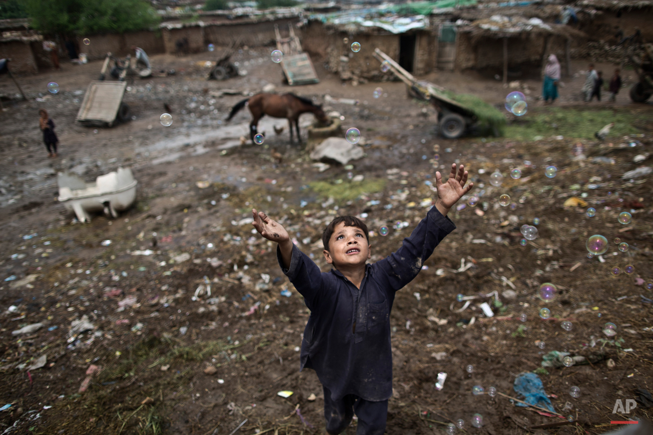 An Afghan refugee child chases bubbles released by other children, while playing on the outskirts of Islamabad, Pakistan, Friday, Aug. 8, 2014. (AP Photo/Muhammed Muheisen)